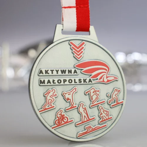 Srebrny, Okrągły Medal z Wypukłym Czerwonym Nadrukiem Przedstawiających Postacie z Różnych Dyscyplin Sportowych